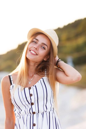 Foto de Young blonde in a hat and summer dress on the beach - Imagen libre de derechos