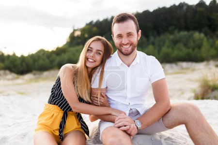 couple amoureux riant assis sur la plage de sable en vacances