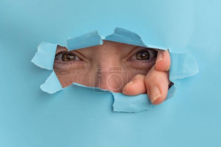 Foto de Mujer mirando a través de un agujero en un cartón roto - Imagen libre de derechos