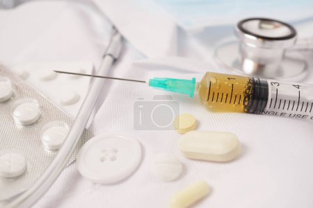 Photo for Syringe, stethoscope and pills on a doctor's gown white background and copy space - Royalty Free Image