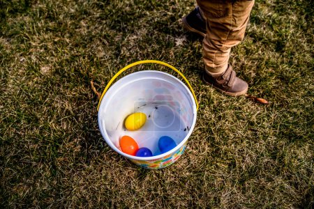 Foto de Niño de pie junto a cubo de plástico lleno de coloridos huevos de Pascua - Imagen libre de derechos