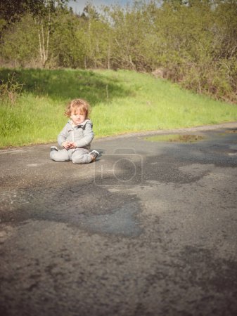 Foto de Un niño pequeño se sienta de rodillas en la carretera después de una tormenta de lluvia - Imagen libre de derechos