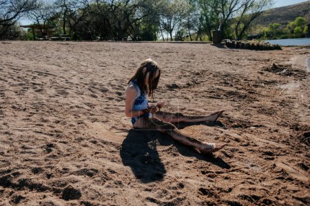 Téléchargez les photos : Fille jouer avec le sable à côté du lac - en image libre de droit