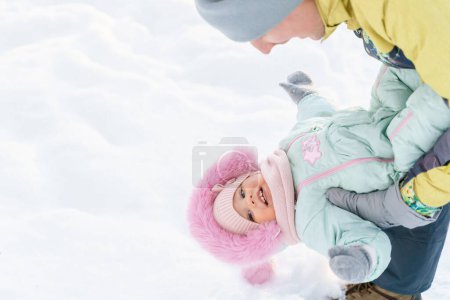 Foto de Padre e hija de un año caminan en un parque cubierto de nieve - Imagen libre de derechos
