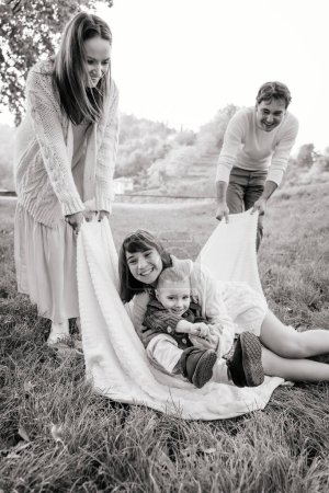 Téléchargez les photos : Image B & W d'une famille heureuse avec deux enfants jouant sur l'herbe - en image libre de droit