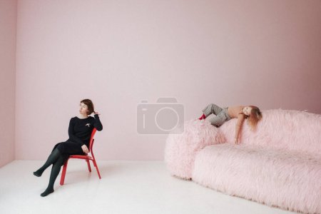 Téléchargez les photos : Femme sur chaise avec fille sur fond rose - en image libre de droit