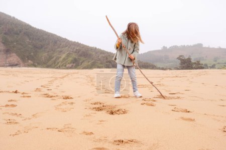 Téléchargez les photos : Petite fille écrit sur une plage de sable avec un tronc d'arbre - en image libre de droit