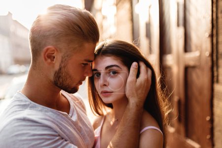 Téléchargez les photos : Jeune homme blond dans un T-shirt étreint une fille dans une robe au coucher du soleil - en image libre de droit