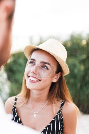 Téléchargez les photos : Young blonde woman in a hat looks at her partner on a sunny beach - en image libre de droit