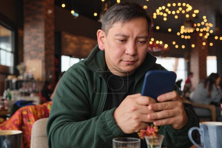 Photo for Asian man in a restaurant in a ski resort with a mobile phone - Royalty Free Image