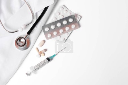 Téléchargez les photos : Stethoscope, pills and syringe on a doctor's gown on a white background and copy space - en image libre de droit