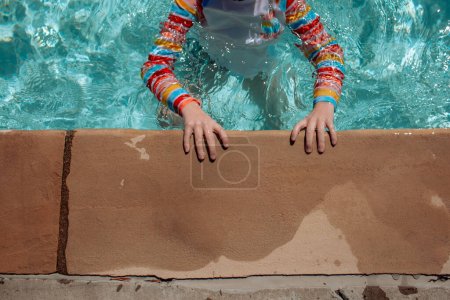 Téléchargez les photos : Jeune enfant tenant sur le côté de la piscine - en image libre de droit