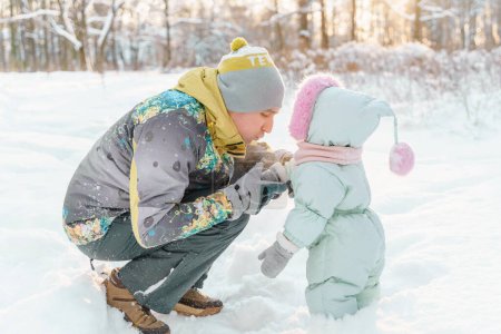 Foto de Padre e hija de un año caminan en un parque cubierto de nieve - Imagen libre de derechos