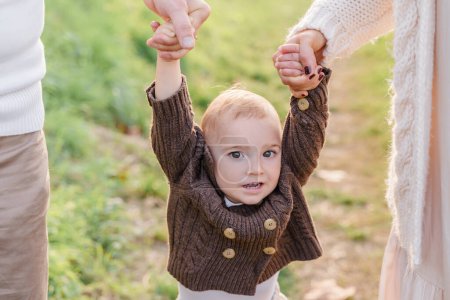 Téléchargez les photos : Maman et papa tiennent le petit garçon par les bras et le conduisent dehors - en image libre de droit