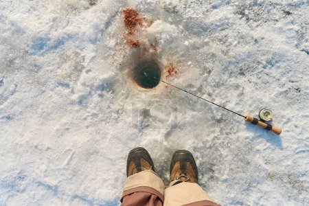 Téléchargez les photos : La canne à pêche se trouve sur la neige à côté du trou, vue de dessus - en image libre de droit