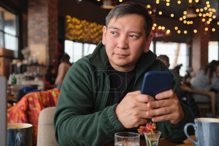 Téléchargez les photos : Asiatique homme dans un restaurant dans une station de ski avec un téléphone portable - en image libre de droit