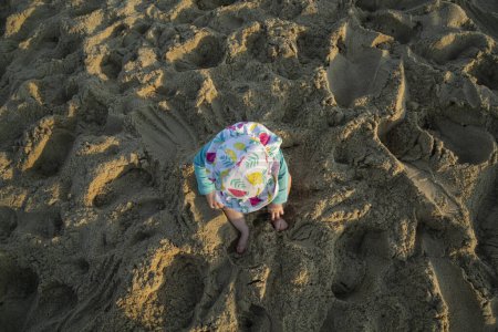 Foto de Vista desde arriba de la niña con sombrero sentado en una playa de arena - Imagen libre de derechos