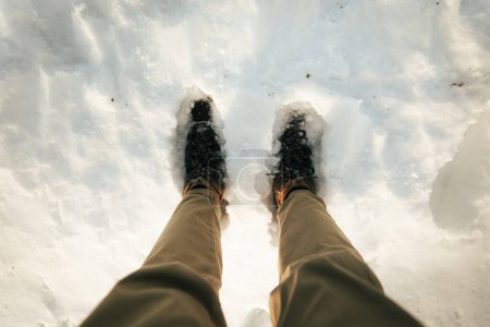 Téléchargez les photos : Jambes d'un homme avec des bottes de randonnée marchant sur un sol plein de neige - en image libre de droit