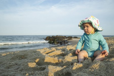 Foto de Retrato de una niña usando un sombrero de sol sentado en una playa de arena - Imagen libre de derechos