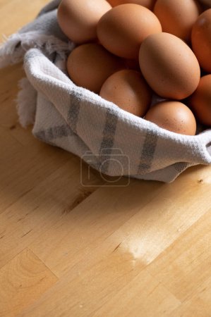 Téléchargez les photos : Œufs bruns sur le comptoir en bois de cuisine enveloppé dans une serviette - en image libre de droit