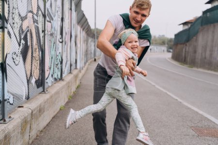 Foto de Papá tuerce a su hija en sus brazos en una calle urbana vacía - Imagen libre de derechos