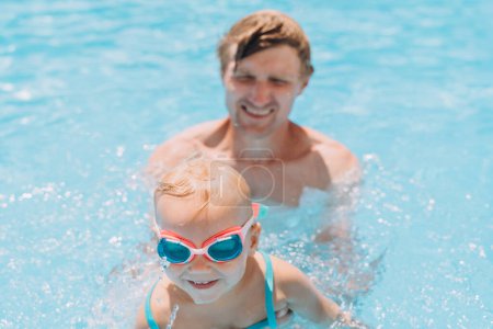 Téléchargez les photos : Papa enseigne à une fille de deux ans à nager dans la piscine extérieure - en image libre de droit