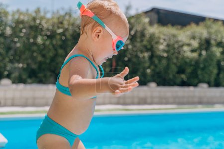 Téléchargez les photos : Une fille de deux ans saute du côté dans la piscine extérieure - en image libre de droit