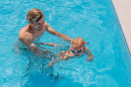 Photo for A man holds a little girl in his arms they swim in an outdoor pool - Royalty Free Image