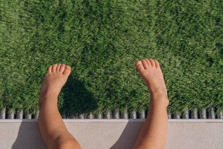 Téléchargez les photos : Les jambes d'une petite fille assise près de la piscine sur la pelouse - en image libre de droit