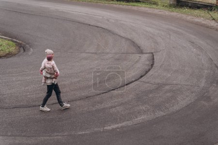 Téléchargez les photos : Un homme marche avec sa petite fille le long d'une route asphaltée montagneuse - en image libre de droit