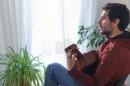 Photo for Man playing Spanish guitar next to the window - Royalty Free Image