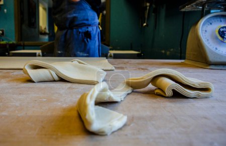 Foto de Tiras de masa de pastelería yacen en el mostrador de madera enharinada en la cocina de panadería - Imagen libre de derechos