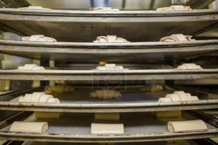 Photo for Racks of uncooked pastry dough sit on stacks of cookie sheets - Royalty Free Image