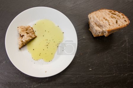 Foto de Un pedazo de pan y aceite de oliva amarillo brillante reposan en un plato blanco - Imagen libre de derechos