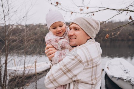 Photo for Dad hugs his two-year-old daughter and smiles outside in late autumn - Royalty Free Image