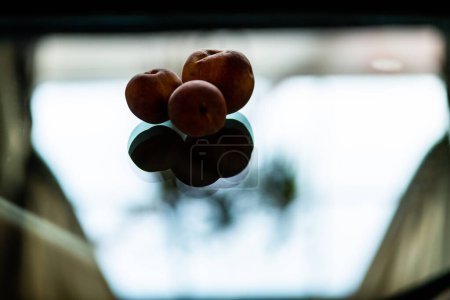 Photo for 3 Peaches on glass table casting reflection - Royalty Free Image