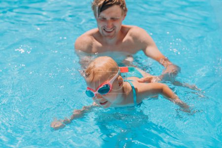 Téléchargez les photos : Papa enseigne à une fille de deux ans à nager dans la piscine extérieure - en image libre de droit