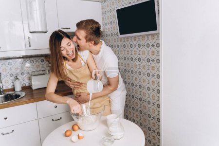 Foto de Una pareja cariñosa cocina panqueques en la cocina y abrazos - Imagen libre de derechos