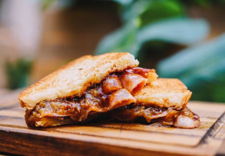 Foto de Sándwich de desayuno con tocino, queso y salsa de tomate sobre tabla de madera - Imagen libre de derechos