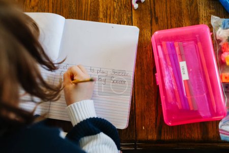 Foto de Hija escribiendo palabras de ortografía junto a la caja de lápiz rosa - Imagen libre de derechos