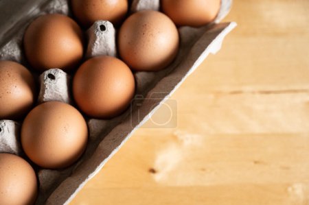 Téléchargez les photos : Gros plan d'un carton d'œufs bio marron sur une table de cuisine en bois - en image libre de droit