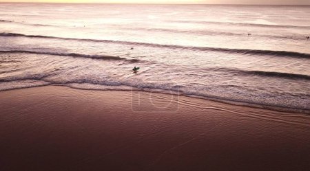 Téléchargez les photos : Lever de soleil majestueux de l'océan avec surfeur solo marchant dans l'eau - en image libre de droit