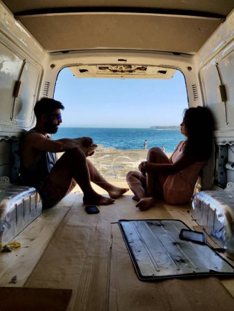 Téléchargez les photos : Couple relaxant assis à l'arrière d'une camionnette devant l'océan. - en image libre de droit