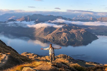 Téléchargez les photos : Homme montant la montagne pendant le coucher du soleil au-dessus des nuages en Nouvelle-Zélande. - en image libre de droit