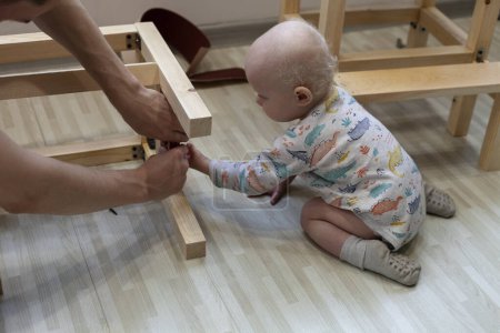 Téléchargez les photos : Enfant tend la main et aide son père à construire une chaise en bois - en image libre de droit