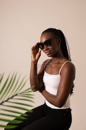 Foto de Modelo femenino negro con gafas de sol y una hoja de palma en el estudio - Imagen libre de derechos