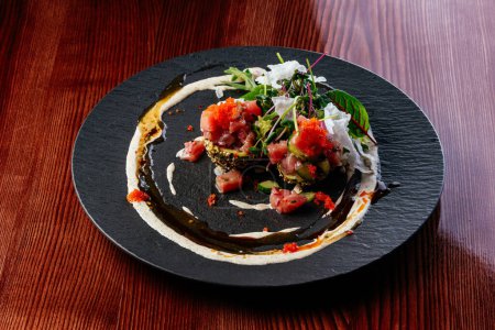 Téléchargez les photos : Tartare de saumon avec sauce et herbes sur une assiette noire - en image libre de droit