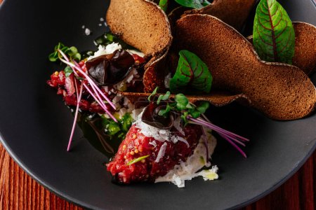 Photo for Beef tartare with sauce and herbs in a black plate - Royalty Free Image