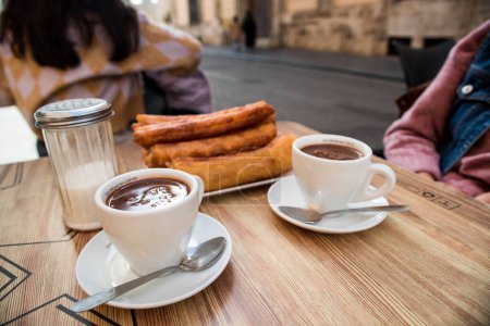 Churros and two cups of chocolate on the terrace table, ready to eat.
