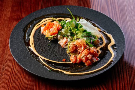 Foto de Tártaro de salmón con salsa y hierbas en un plato negro - Imagen libre de derechos